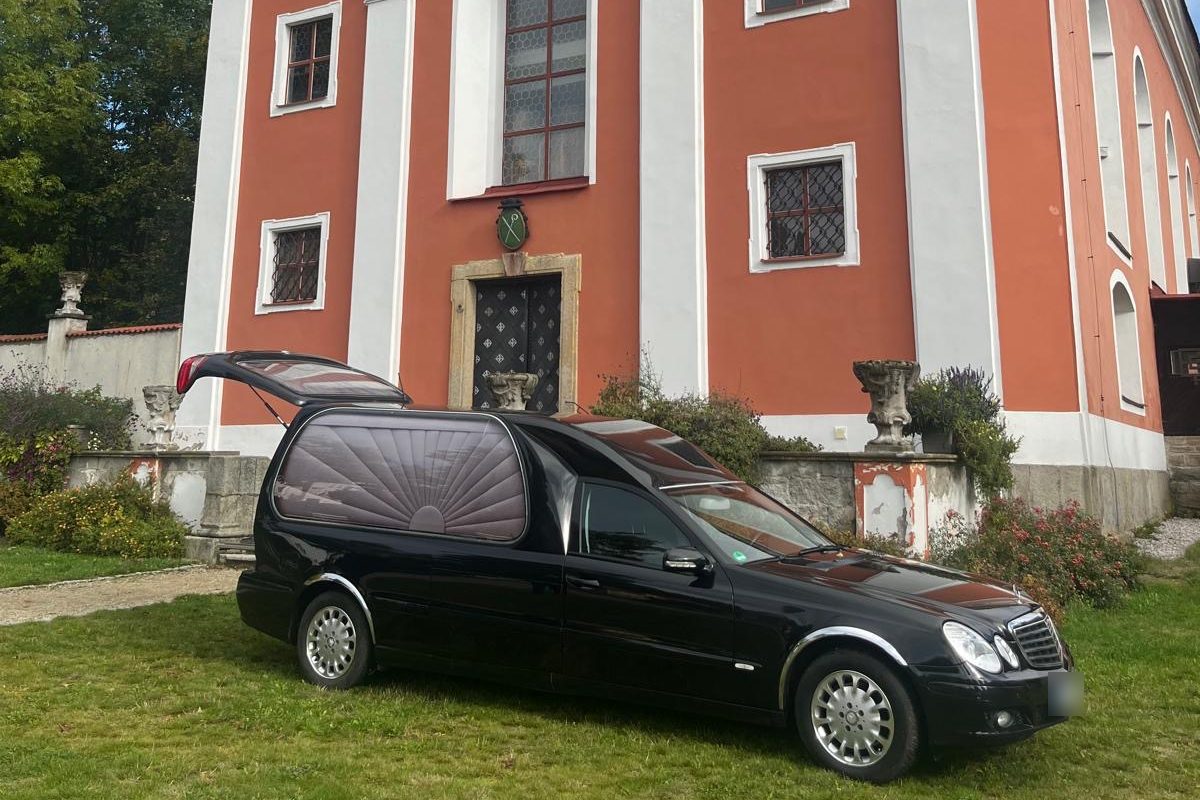 Černý pohřební vůz před barokním kostelem